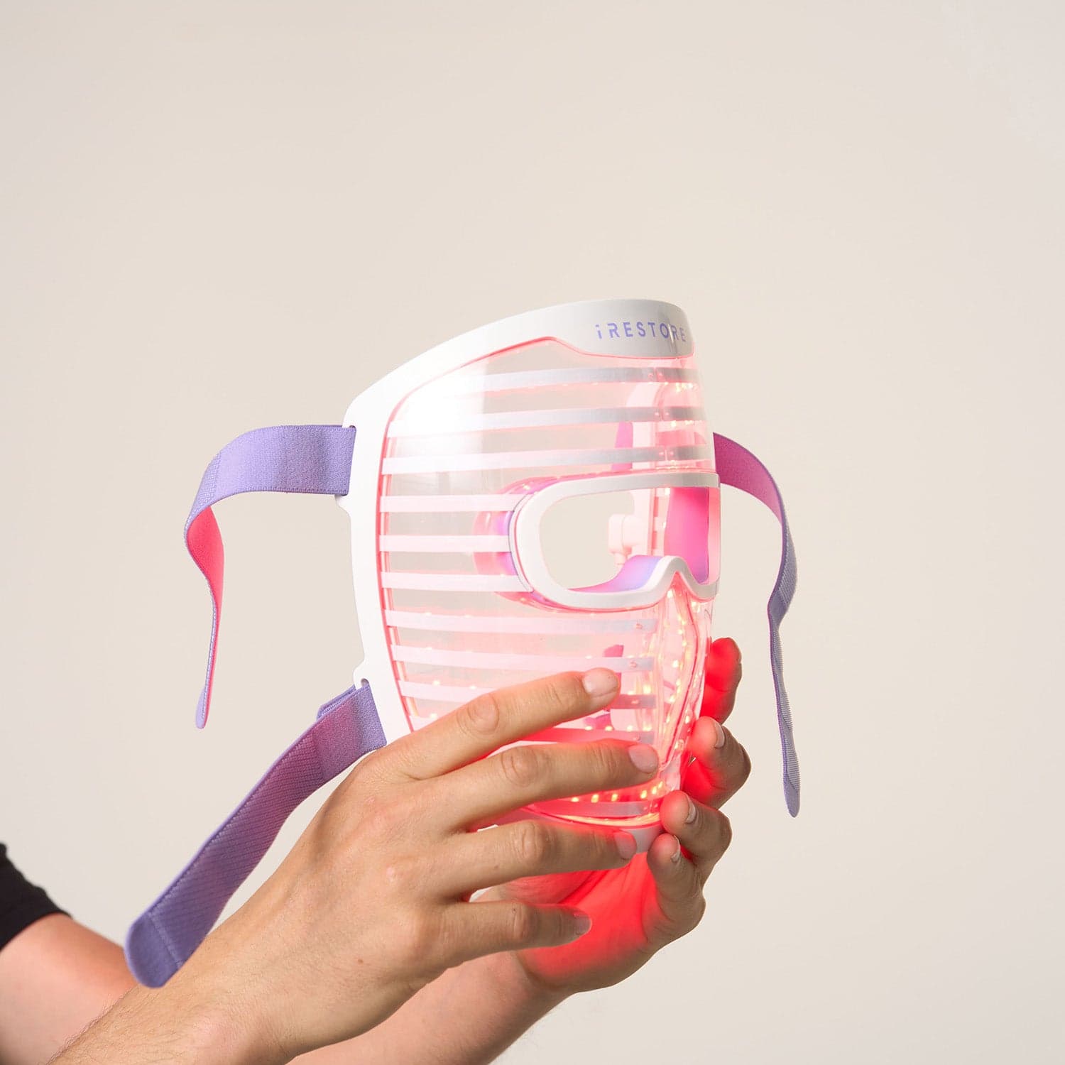 Close-up of hands holding the white iRestore Illumina LED face mask while its red LEDs are lit.