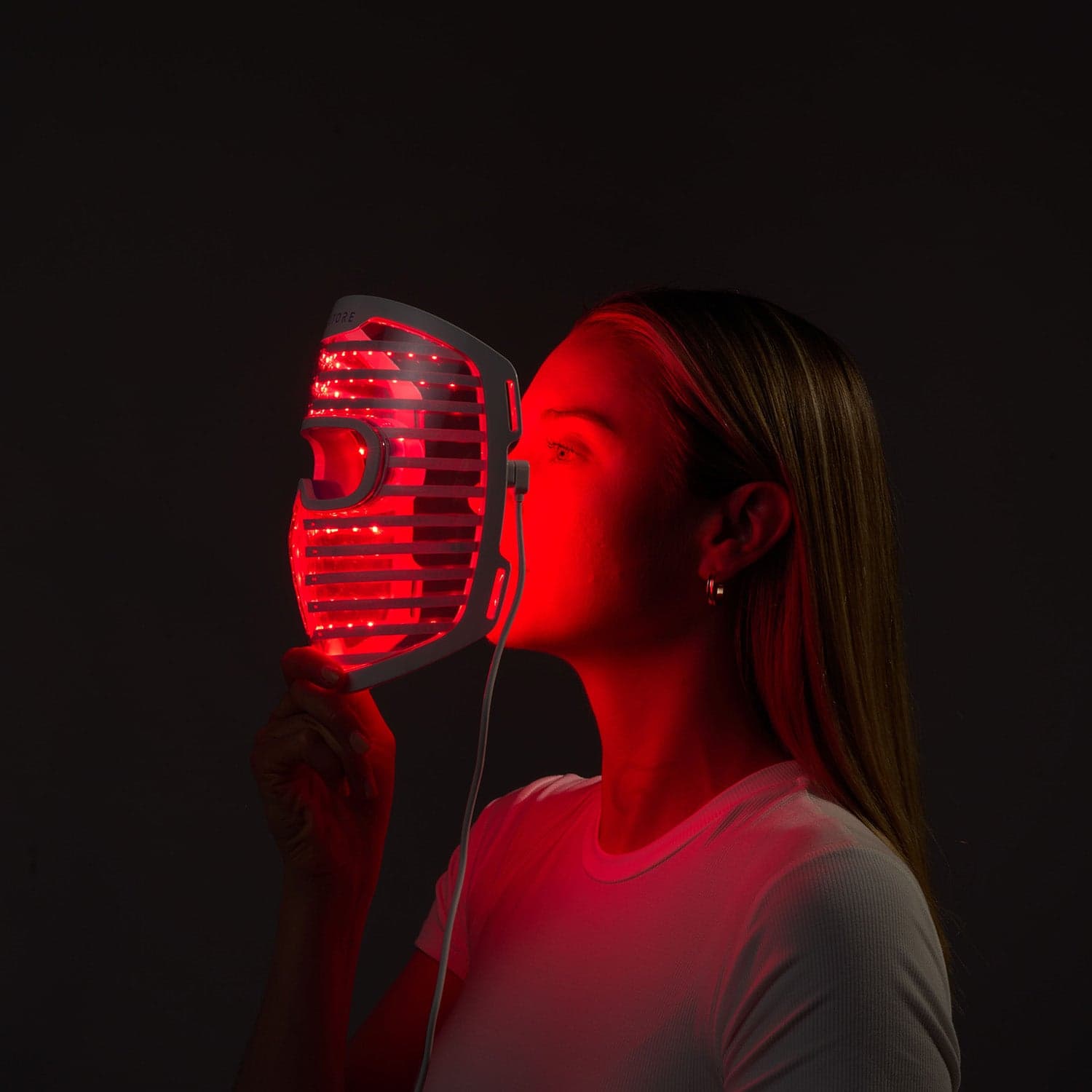 Woman holding the exact white iRestore Illumina face mask with its red LEDs illuminated.